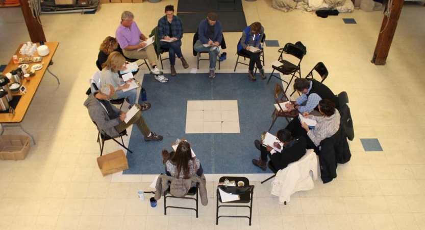 A group of people sit in chairs arranged in a circle during the family seminar of an outward bound intercept course.